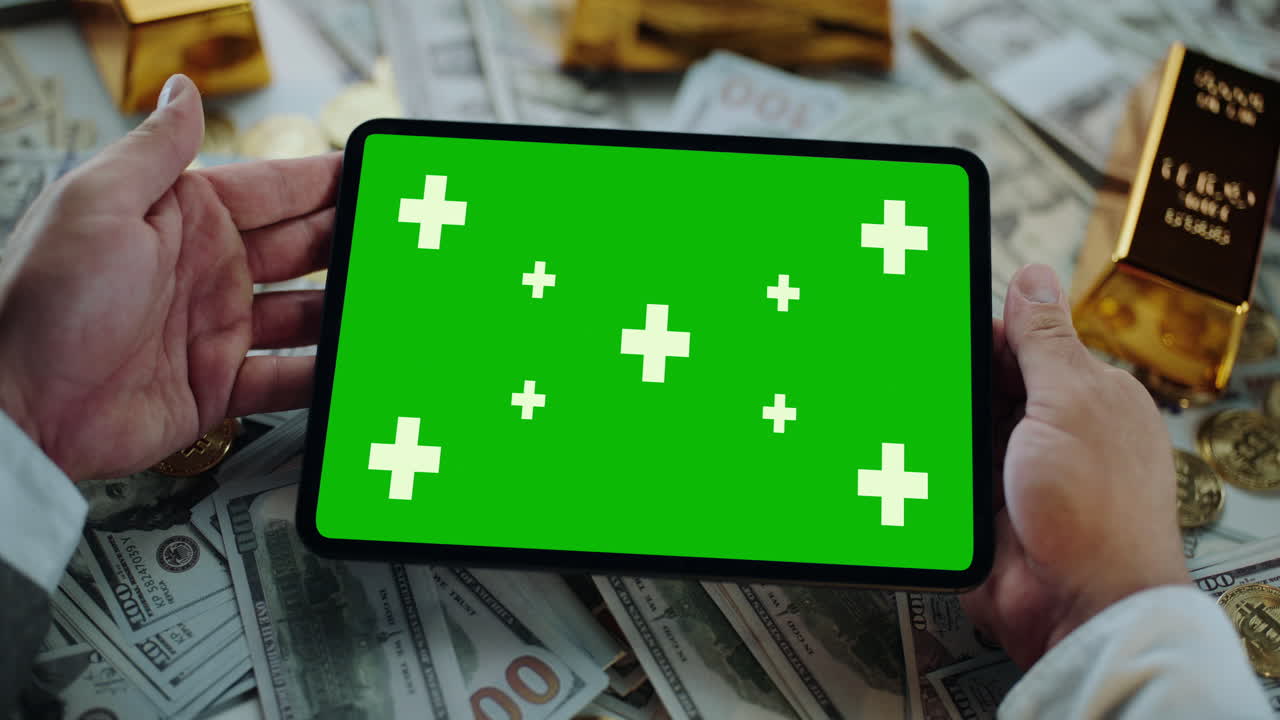 Tablet with Green Screen Display Amidst Money and Gold
