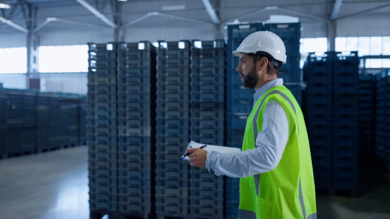 empleado del almacén haciendo notas calculando cajas azules con uniforme verde
