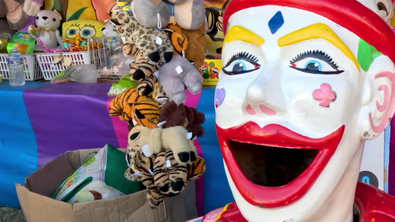 A vibrant clown head statue surrounded by an array of plush toys and colorful decorations.
