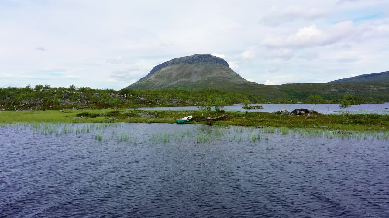 Aerial view over lake Tshahkajarvi, towards boats on the coast, the Saanatunturi fell in the background, on a cloudy, summer day, in Kilpisjarvi, Enontekio, Lapland, Finland