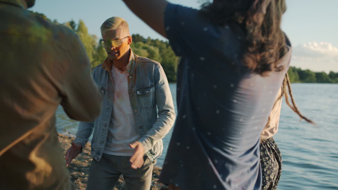 jóvenes locas chicas y chicos sucios con pintura colorida bailando en la playa disfrutando del tradicional festival de holi