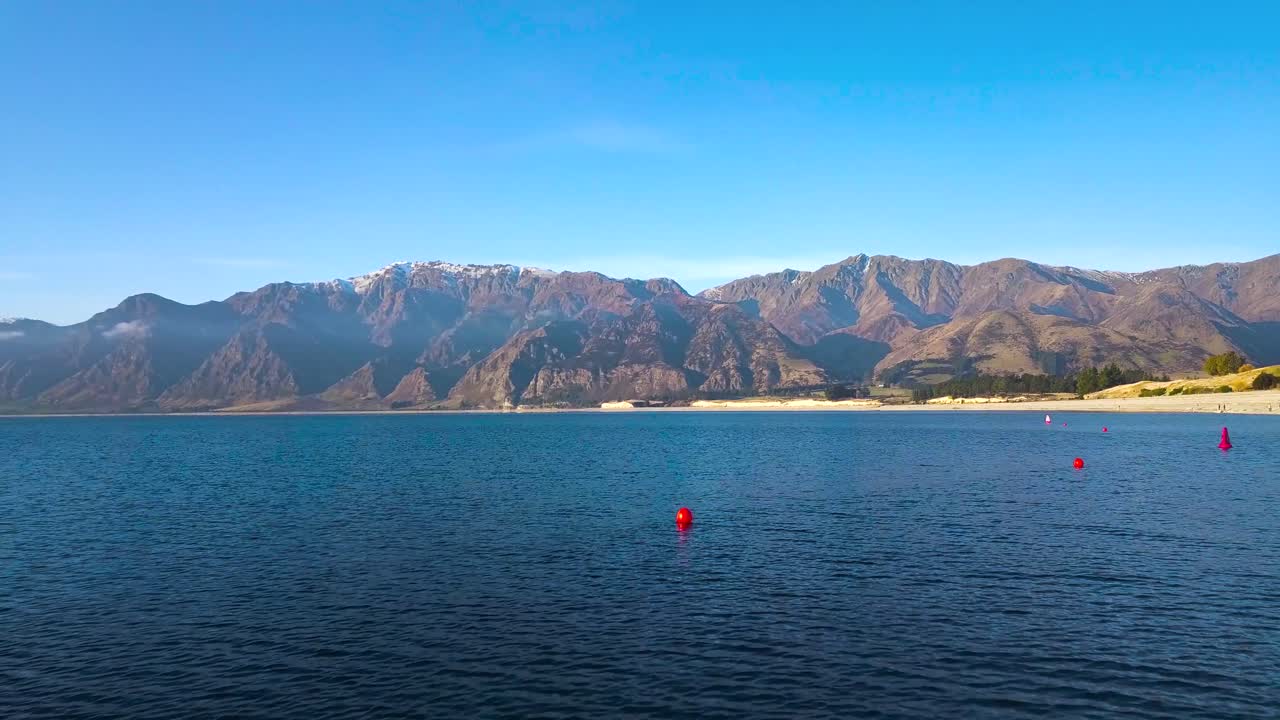 Aerial shot of stunning blue water in Lake Hawea in New Zealand and wild steep hills in the background