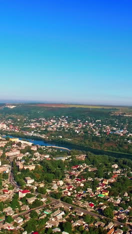 flight above the dense urban landscape on sunny summer daytime. river flowing at backdrop among the green banks. vertical video