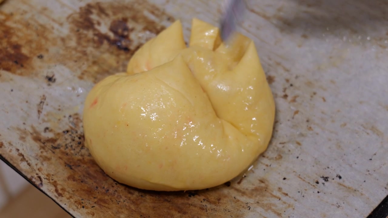 Scissors score a decorative star pattern on a single praline brioche ball