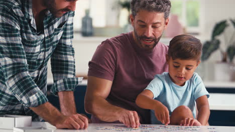 Cerca-De-Una-Familia-Del-Mismo-Sexo-Con-Dos-Padres-Y-Su-Hijo-Haciendo-Rompecabezas-En-La-Cocina-De-Casa