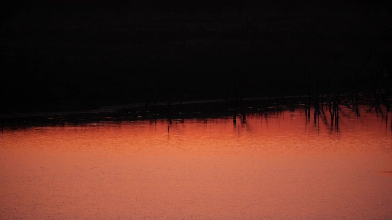 Increspature dell'acqua al rallentatore su un lago che riflette un vibrante tramonto arancione.
