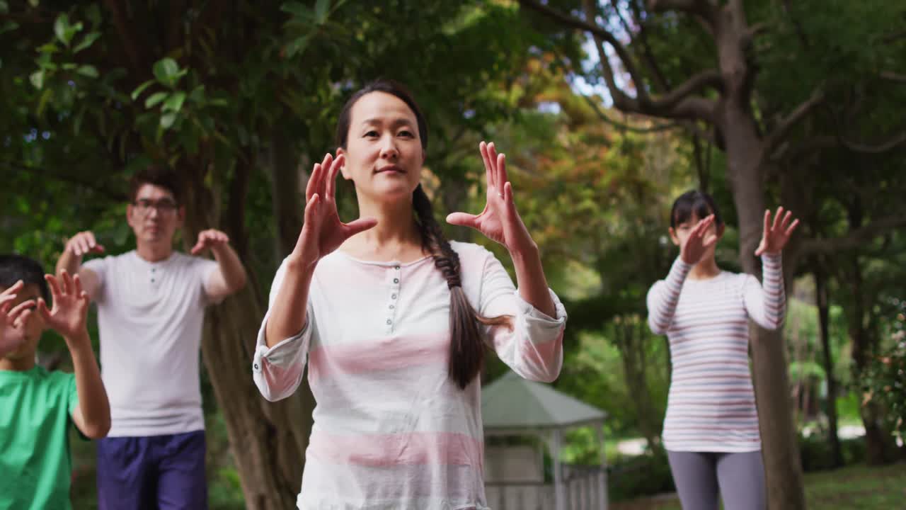 Happy asian parents exercising in garden with son and daughter, practicing tai chi together