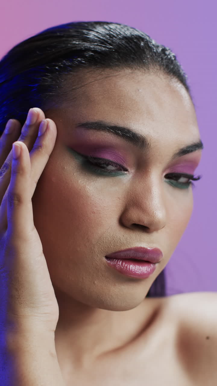 Vertical video of biracial woman with black hair and make up touching face, copy space, slow motion