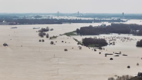 Aerial-panning-shot-of-teh-Waal-River-after-it-has-overrun-its-banks-from-heavy-storms-and-flooding-farm-fields-and-villages,-with-the-Martinus-Nijhoffbrug-bridge-and-Zaltbommel-in-the-background