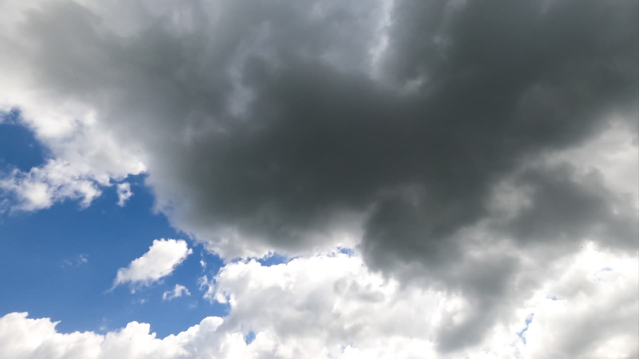 White and grey clouds forming in the blue sky. Rays of sun breaking through the clouds timelapse. View from below.