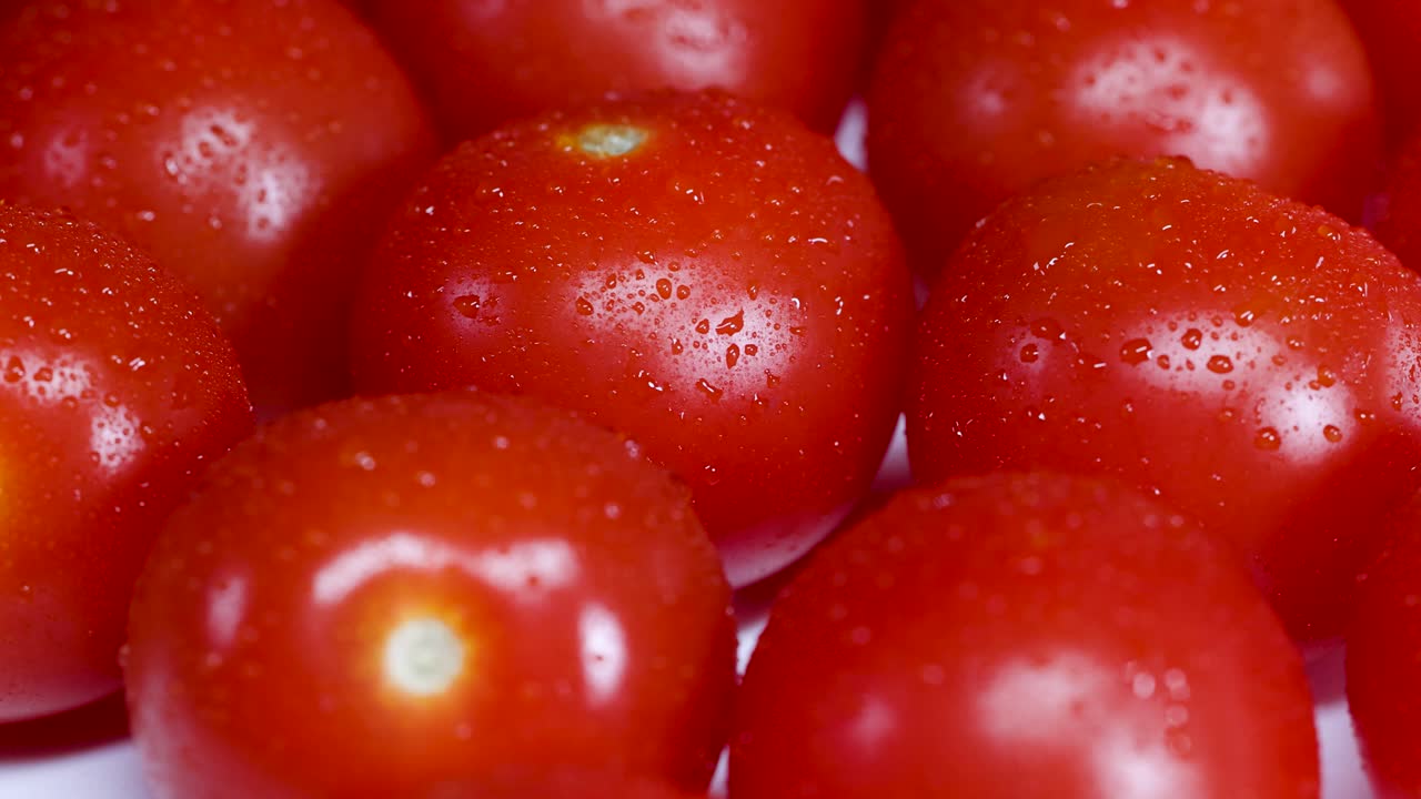 Macro video showcasing vibrant cherry tomatoes with droplets, rotating under bright lighting, emphasizing freshness and texture