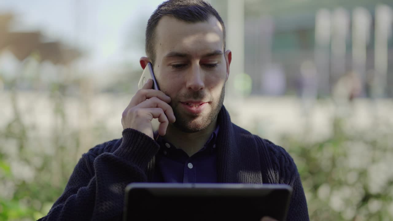 hombre guapo sosteniendo una tableta y hablando en un teléfono inteligente