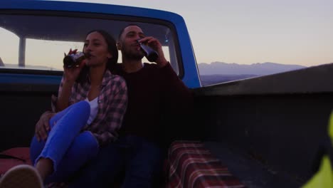 Young-couple-on-a-road-trip-sitting-outside-on-their-truck-at-dusk