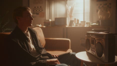 young man relaxing on sofa, listening to music on vintage boombox