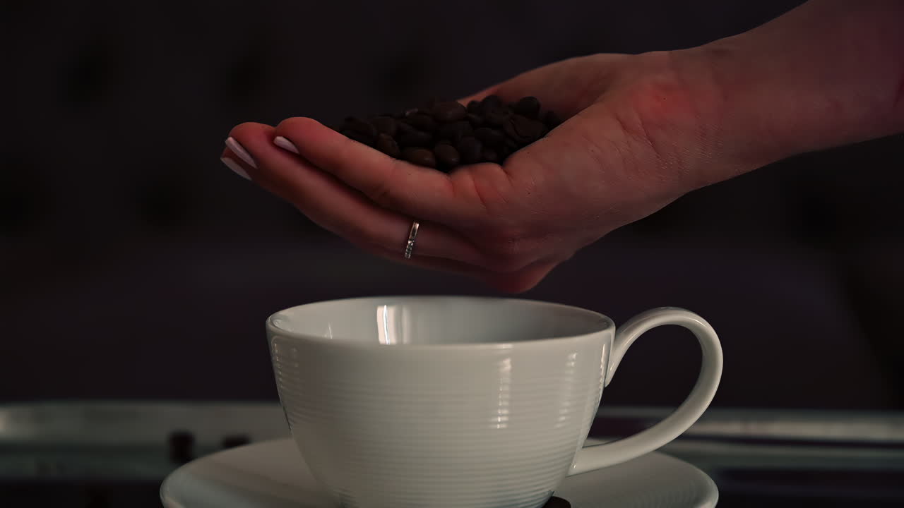 Close up of a woman's hand pouring roasted coffee beans into a white cup