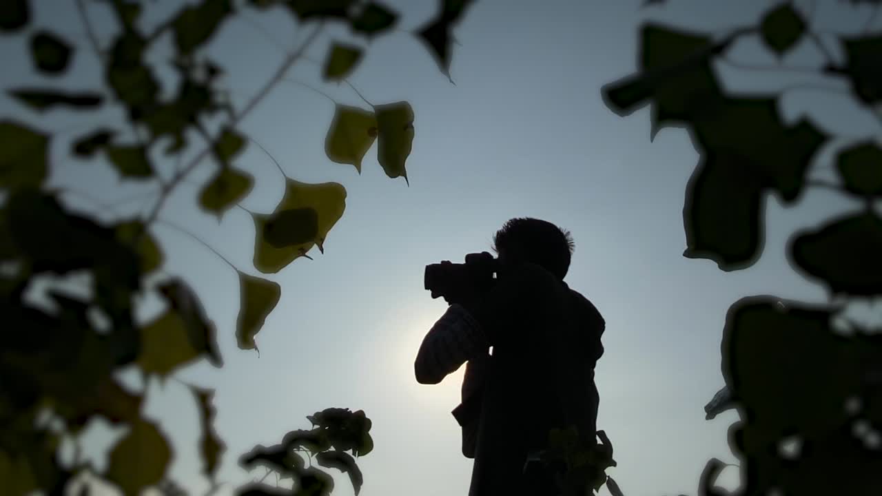 太陽を背景に写真を撮る男性カメラマンのシルエット