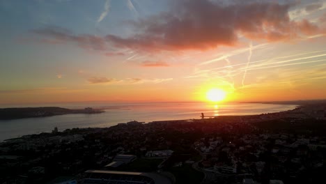 Una-Espectacular-Vista-Aérea-De-Una-Puesta-De-Sol-Sobre-El-Océano-Con-Una-Ciudad-Costera-En-Primer-Plano