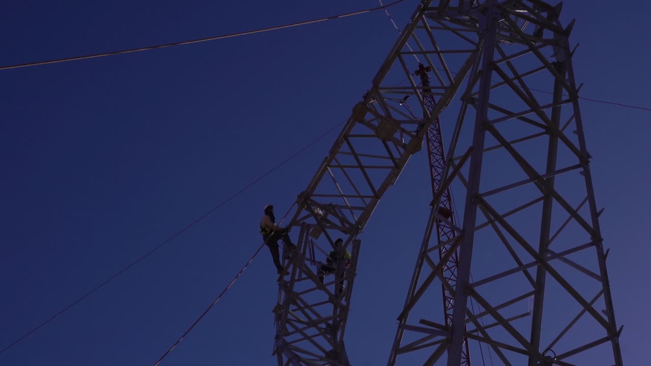 técnicos trabajando a grandes alturas en una torre eléctrica de alta tensión, contra el cielo azul