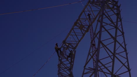 Técnicos-Que-Trabajan-A-Grandes-Alturas-En-Una-Torre-Eléctrica-De-Alta-Tensión,-Contra-El-Cielo-Azul