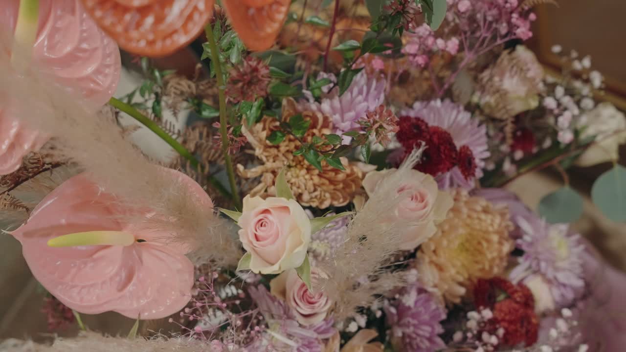 Nærbillede af pastelbuket med lyserøde anthurium, roser, krysantemum, tørrede teksturer og grønt