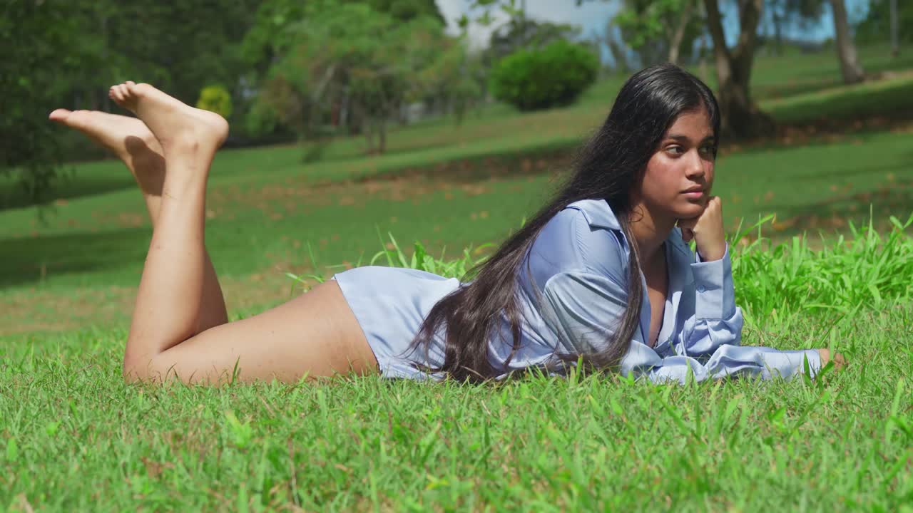 молодая восточно-индийская девушка в синей рубашке в парке, лежащая в траве