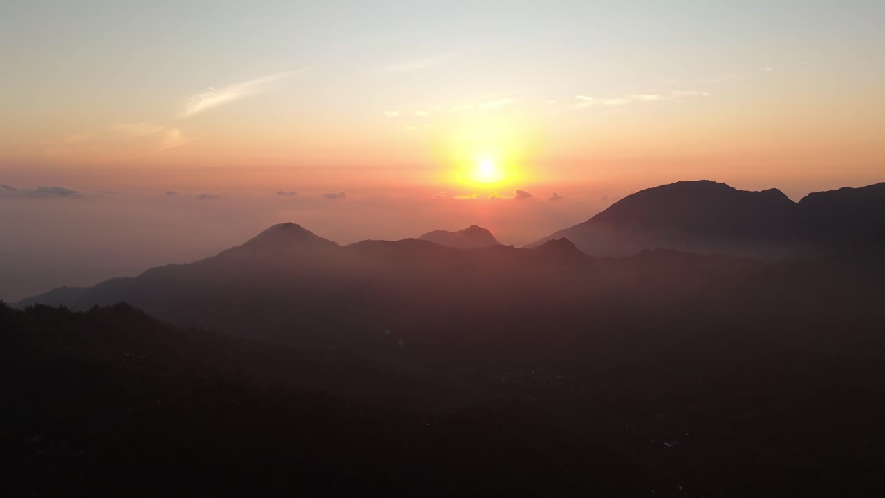 Sunset over mountain peaks in Karangasem, Bali with orange sky and distant tropical horizon, misty sky