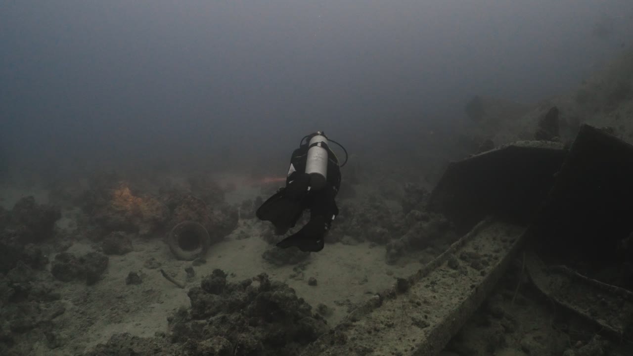 Scuba diver with flashlight swimming between wreckage on the sea bottom in 4k