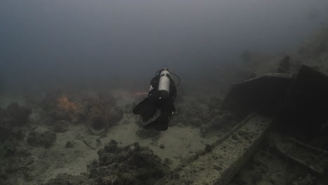 scuba diver with flashlight swimming between wreckage on the sea bottom in 4k