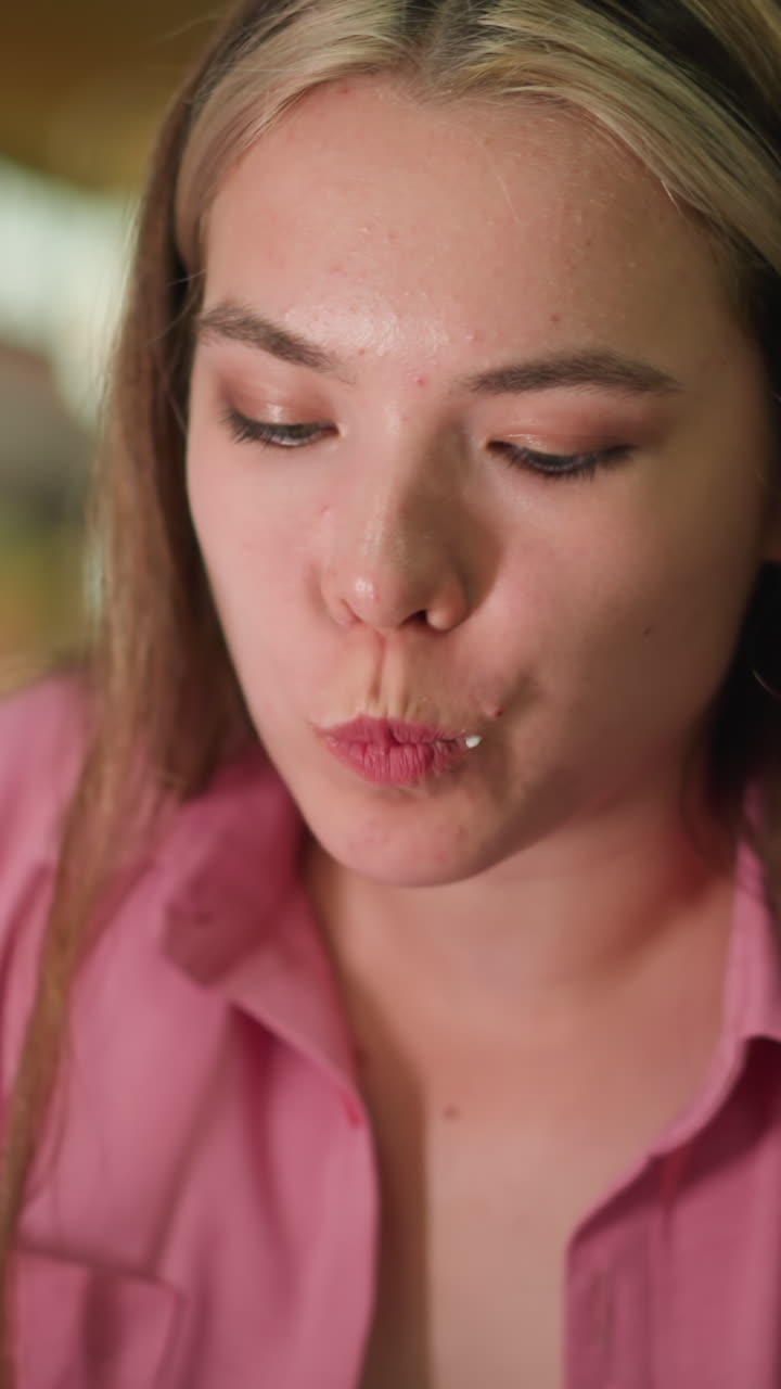 la dama de vestido rosa toma un bocado de hamburguesa, masticando lentamente, asintiendo con la cabeza con satisfacción debido al delicioso sabor. parece reflexiva mientras saborea la comida, con un fondo borroso