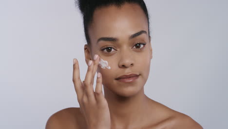 portrait beautiful young african american woman applying skin cream moisturizer on face enjoying exfoliation massaging luxury anti aging lotion perfect feminine beauty on white background skincare concept