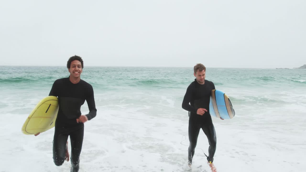 vista frontal de dos surfistas masculinos corriendo juntos con una tabla de surf en la playa 4k