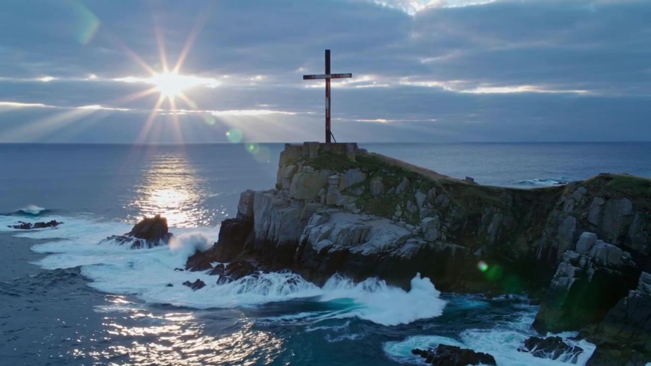 Mostra un promontorio roccioso sormontato da una grande croce eretta, il sole che emerge tra le nuvole, le onde che si infrangono.