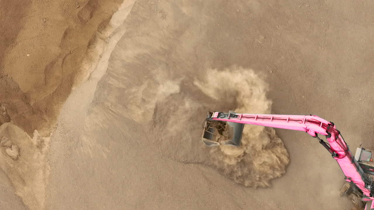 A close-up aerial shot of an excavator's bucket scooping sand, creating a cloud of dust and highlighting the texture