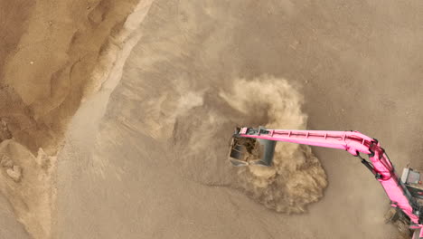 a close-up aerial shot of an excavator's bucket scooping sand, creating a cloud of dust and highlighting the texture