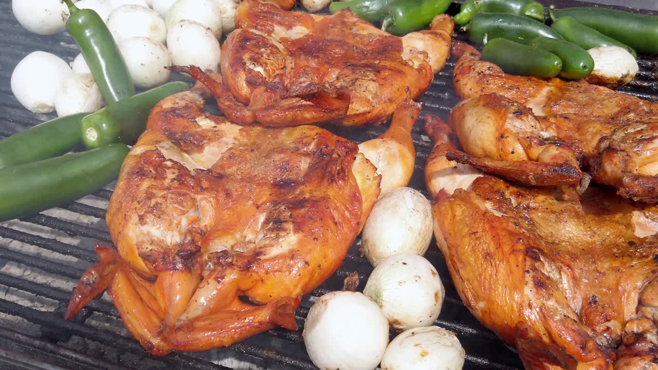 Close-up of grilled chicken, onions, and jalapeño peppers sizzling on a barbecue grill. Traditional Mexican street food “pollo asado” cooked over open flame