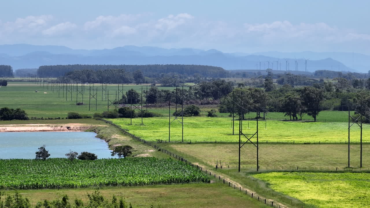 Telephoto 7x view of high voltage transmission lines across farmland with distant wind turbines