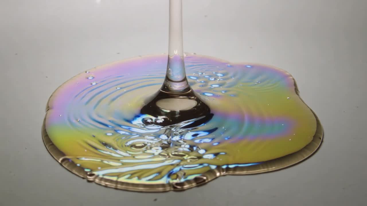 液体柱がプレート上の膜の液だまりに接触し、科学的な研究のために波紋と虹色の帯を作り出す。