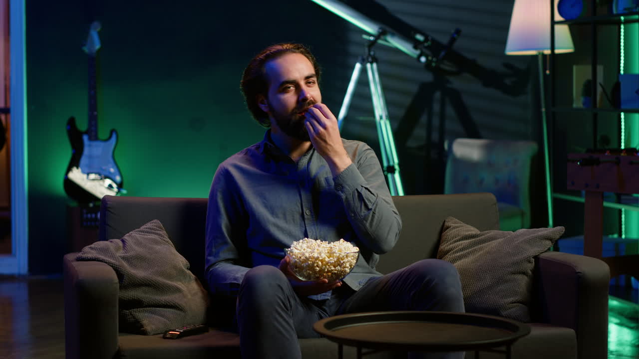 hombre encendiendo la tv usando el control remoto, comiendo palomitas de maíz