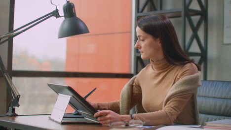 a female graphic designer works in an office with large windows and paints using a stylus and a computer touch screen. workstation with touchscreen for designers. come up with and develop the concept of the logo.