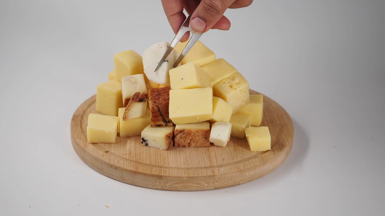 Hand Picking a Cheese Cube from Assorted Cheeses on a Wooden Board