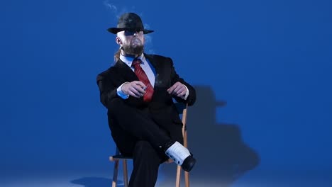 man in suit and hat smoking on blue background