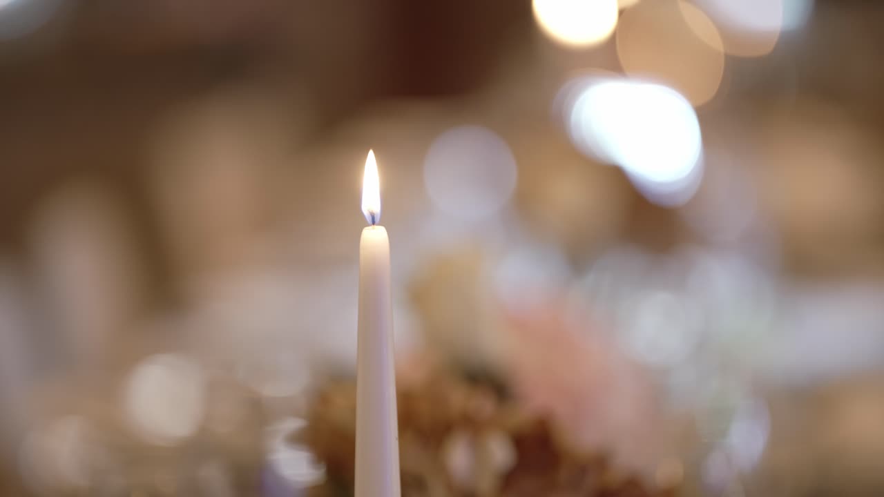lit white candle with soft bokeh lights in background at elegant wedding table