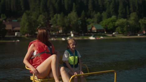 glad young mother and daughter sit in catamaran. smiling woman and girl talk relaxing on lake on sunny day slow motion. family summer vacation