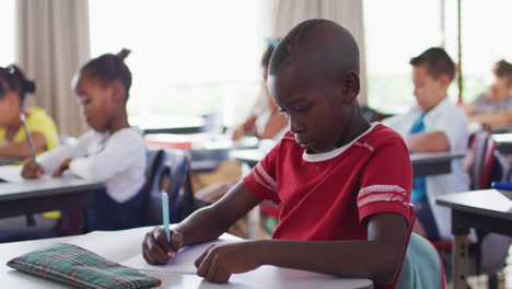 Porträt-Eines-Afroamerikanischen-Schuljungen,-Der-Im-Klassenzimmer-Sitzt-Und-Notizen-Macht