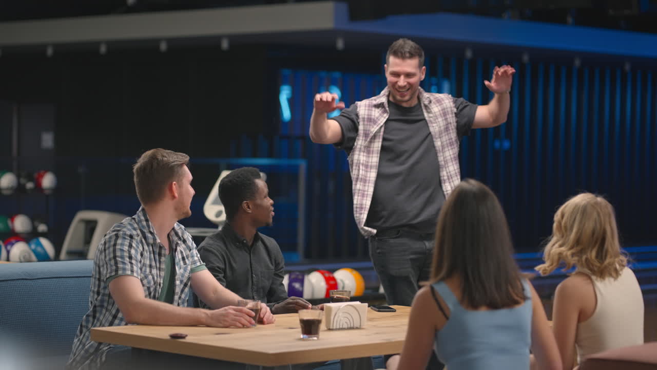 A cheerful man in a bowling club happily runs to his friends to celebrate the knocked out air. Share the victory with friends. Multi-ethnic group of friends