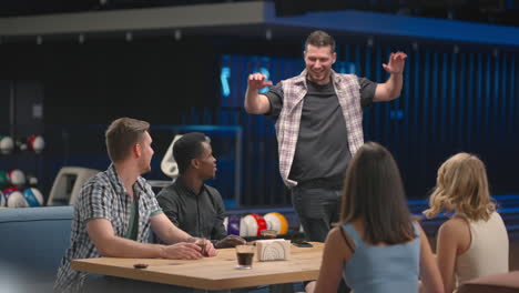 a cheerful man in a bowling club happily runs to his friends to celebrate the knocked out air. share the victory with friends. multi-ethnic group of friends