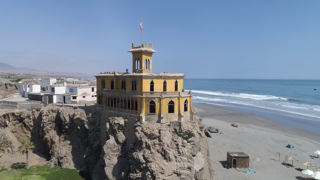 A stunning yellow mansion stands abandoned on a rocky cliff, overlooking the vast blue ocean. Perfect for travel, history, and cinematic scenery. Mollendo, Arequipa, Peru.