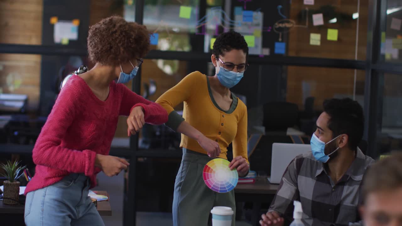 Diverse colleagues wearing face masks greeting each other by touching elbows at modern office