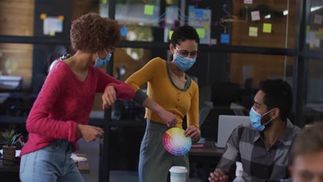 diverse colleagues wearing face masks greeting each other by touching elbows at modern office