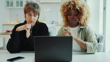 two young female friends using laptop and talking at home
